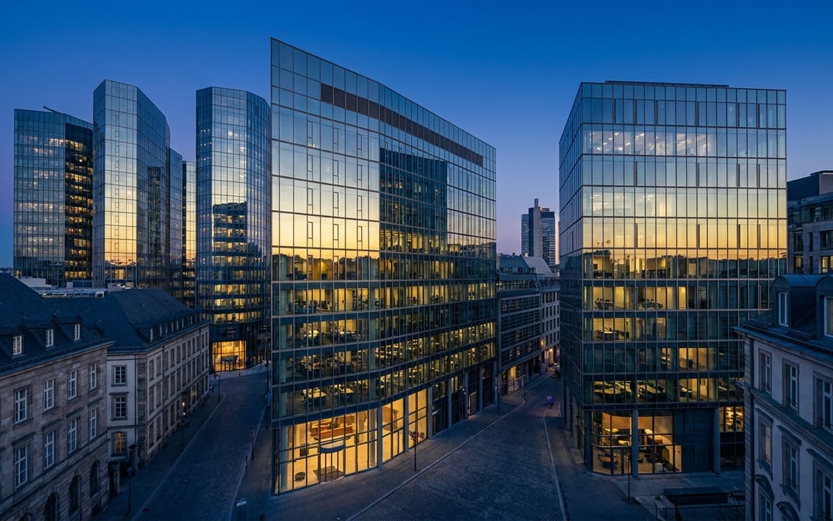 Glass office towers reflecting a low evening sun in a European financial district